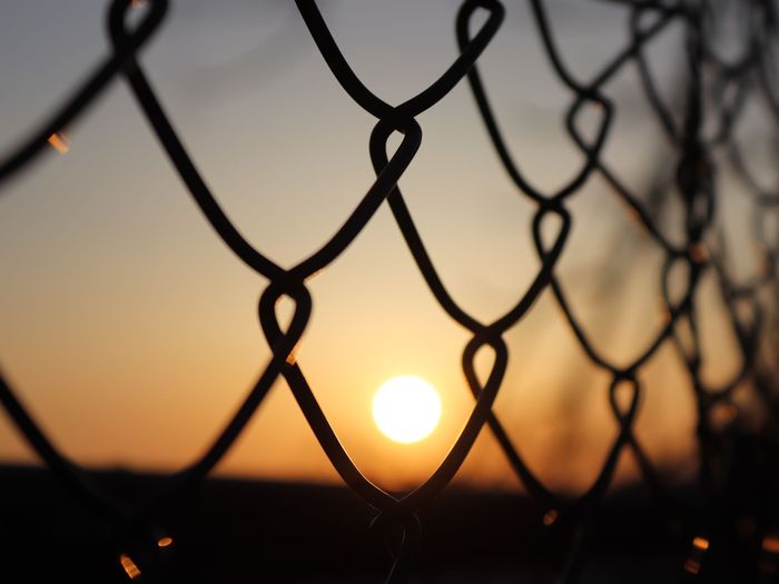 A chain-link fence with the sun setting behind it